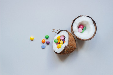 Ripe coconut with colorful sweets on the gray background, top view