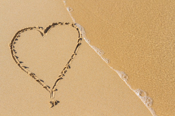 Heart drawn on a sand of beach with the wave of the sea in the morning with place for your text. Summer holiday concept. Romantic love background. Valentine's Day theme. Top view. Copy space.