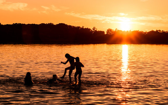 Kids and families are having fun at a lake under sunset