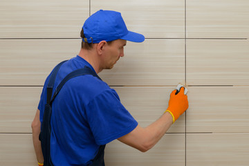 master-tiler blocks the seams between the tiles with beige cement grout