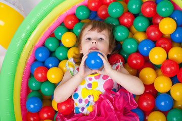 Fototapeta na wymiar Маленькая девочка играет в сухом бассейне. Девочка держит мяч