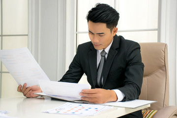 Young businessmen who is wearing black jacket is reading and checking the information on the documents at the office