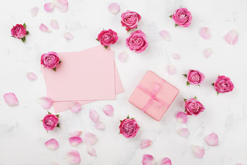 Fototapeta na wymiar Gift or present box, envelope, paper blank, petals and pink rose flower on white table top view in flat lay style. Greeting card on Womans day.