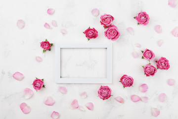 Wedding mockup with white frame, pink rose flowers and petals on light table top view. Beautiful floral pattern. Flat lay style.