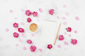 Morning coffee cup for breakfast, empty notebook, pencil and pink rose flowers on white stone table top view in flat lay style. Woman working desk.