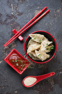 Above view of red tableware with steamed gyoza on a brown stone background