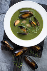 Spinach soup with mussels and green olives served in a white plate, view from above, vertical shot