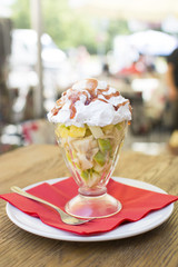 Sweet tasty fruit salad in the bowl with whipped cream on the wooden table.