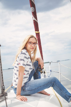 Slim blonde in jeans sitting on nose of white yacht