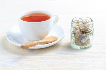 A cup of green tea with chamomile in a jar and a wooden spoon