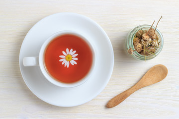 Tea with chamomile on a white wooden background with a jar and a spoon