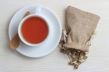 A cup of tea with a bag of chamomile and a wooden spoon.
