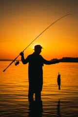 A fisherman with a fishing rod in his hand and a fish caught stands in the water against a...