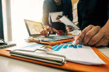 Businessman hand using laptop and tablet with social network diagram and two colleagues discussing data on desk as concept in morning light.
