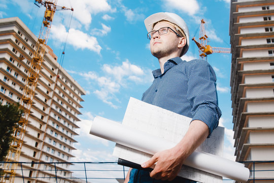 close-up man construction builder worker - foreman is engineer in protective helmet, glasses on the background of building house with crane. Concept calculation construction time, cost.