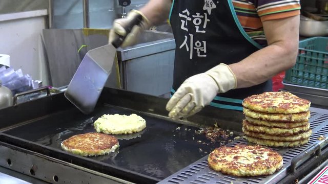 4K Bindae-tteok in Gukje International Market Busan city. Bindaetteok, fried buchimgae, savory pancake with ground mung beans, vegetables, meat. Korean vendors selling food in street, South Korea-Dan