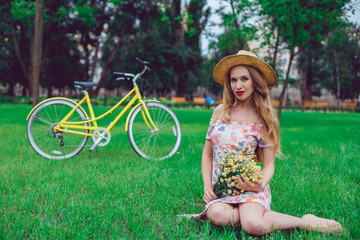 Outdoor portrait of a beautiful blonde woman. Attractive sexy girl in a field with flowers and bike on the background.