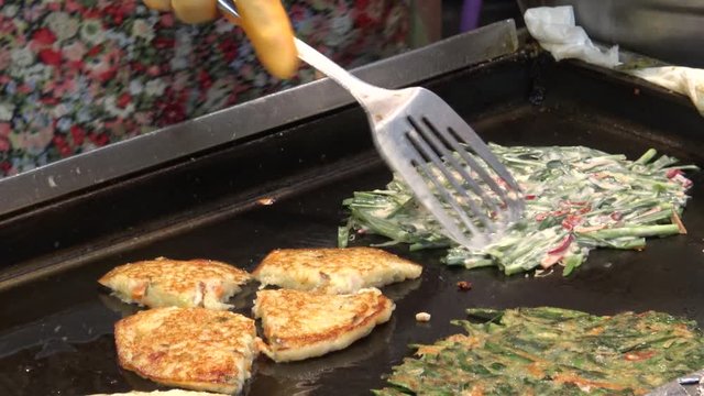 4K Bindae-tteok in Gukje International Market Busan city. Bindaetteok, fried buchimgae, savory pancake with ground mung beans, vegetables, meat. Korean vendors selling food in street, South Korea-Dan
