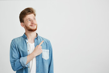 Portrait of cheerful young handsome man smiling pointing finger up over white background.