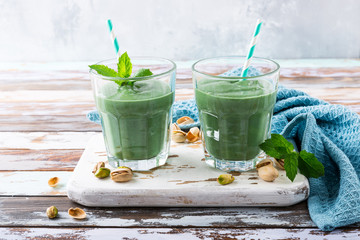 Two glasses of healthy green smoothie with mint, pistachios and spirulina on old wooden background. Detox, diet, healthy, vegetarian food concept with copy space.