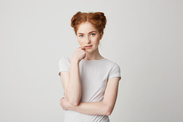 Portrait of young pretty girl with red hair looking at camera touching chin over white background.
