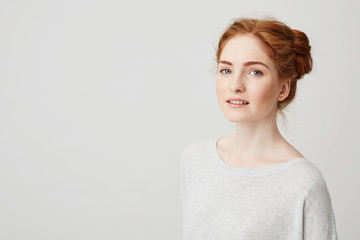 Portrait of beautiful redhead girl with buns and freckles smiling looking at camera over white background.