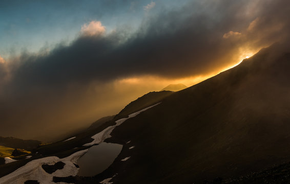 Sunset on mountain lake. Evening landscape. Photo through clouds. Caucasus mountains.