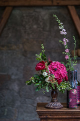 Wedding peony bouquet with wine bottles against vintage dark stone background. Rustic style.
