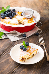 Piece of homemade cheesecake made from cottage cheese, decorated with blueberries and mint on wooden background. Healthy food concept with copy space.