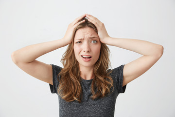 Embarrassed young pretty girl holding her head looking at camera over white background.