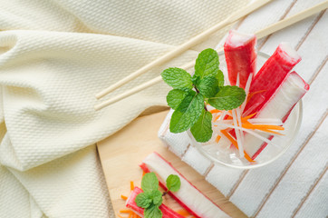 Crab stick with sliced carrot and radish in a glass on fabric background.