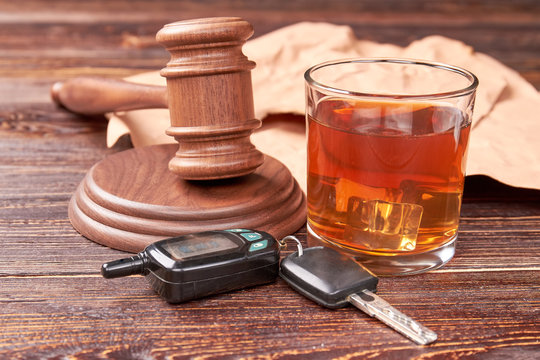 Drunk driving concept. Driving keys, gavel, glass of whisky on wooden background. Drink and drive is hard crime.