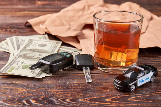 Dollars, keys, whiskey, police car. Glass of whiskey beside of car keys and police car. Money penalty for alcohol drinking.