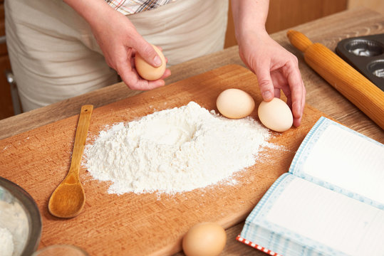 Woman cooking dough. Flour for baking on a wooden background with kitchen utensils. Hands and food closeup. Break an egg.