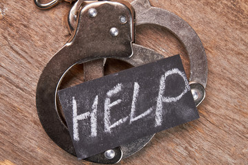 Handcuffs and message close up. Prisoner metal shackles, wooden background. Request of help.