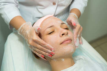 Fototapeta na wymiar Beautiful young girl on facial cleansing procedure at a cosmetologist