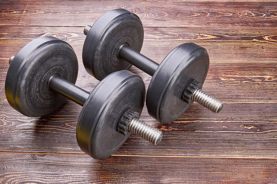 Training dumbbells on wooden floor. Black barbell for lifting in gym.