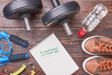 Sound mind in sound body. Paper notebook, jumping rope, dumbbells, water, sport shoes, wooden...