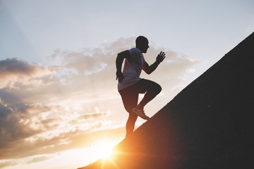 Male runner trains in an ascent to a mountain. Athlete runs through the mountains and hills at...