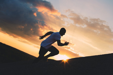 Athlete in sportswear runs up the mountain at sunset. Fitness training at sunset on outdoor