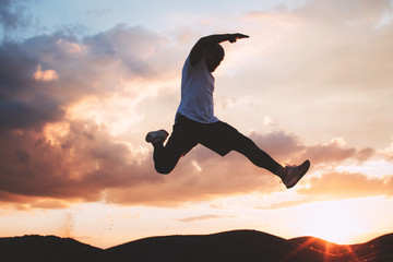 Strong and brave athlete jumps over a ditch. Silhouette of a man at the moment of a jump