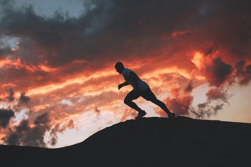 Silhouette of a sporty man running down the hills. Running at sunset