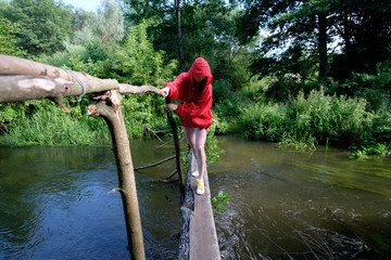 girl in red waterproof jacket fording river over handmade bridge