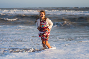girl in a skirt playing on the sandy shore before a stormy sea