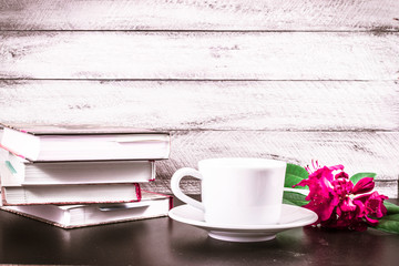 Stack of books, cup of coffee and Rhododendron flowers on wooden background. cover, card. copy space.