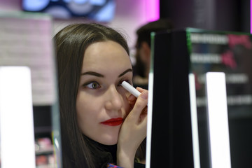 Beautiful brunette with red lipstick is testing the eyeshadows in beauty store