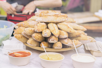 Close-up of fresh hot baguettes and diffrent sauces for sandwiches, selective focus. Hands of seller in the background with money. Real scene in market.