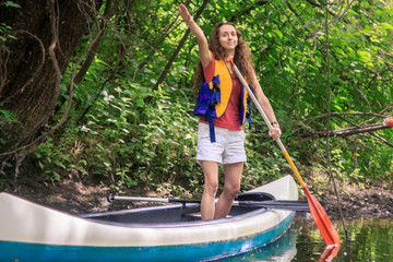 A young girl showing direction on a kayak with a paddle in a forest on a stream with lianas