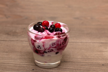Raspberries, blueberries, blackberries mixed with natural yogurt inside a small glass on a wooden table