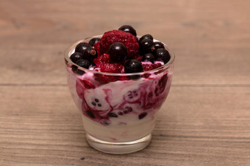 Raspberries, blueberries, blackberries mixed with natural yogurt inside a small glass on a wooden table